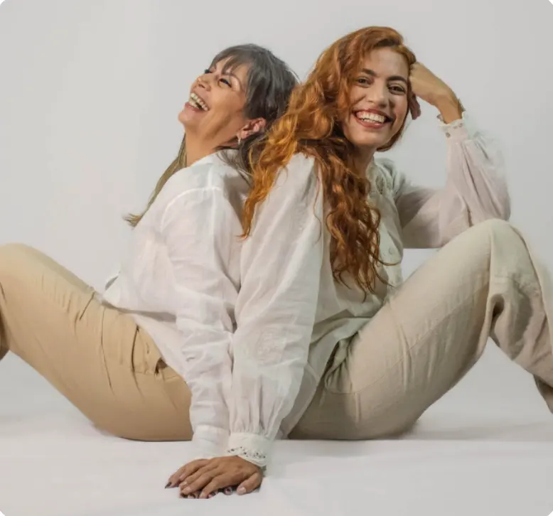 Duas mulheres sorrindo, sentadas no chão do estúdio