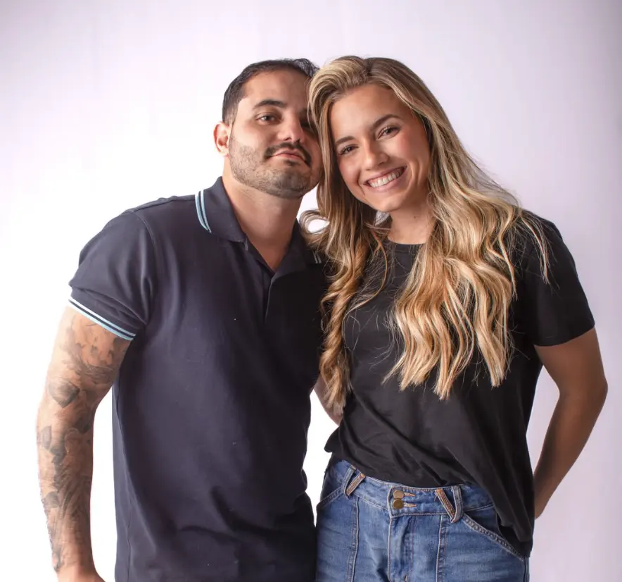 Casal abraçado e sorrindo em ensaio no estúdio, sobre fundo claro